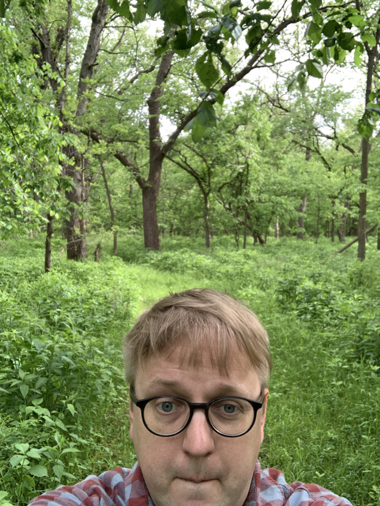 Photo of Nolan Tredway, facing the camera in front of a back drop of green forest